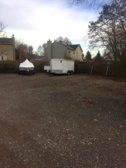 An enclosed cargo trailer and a covered boat parked along the fence